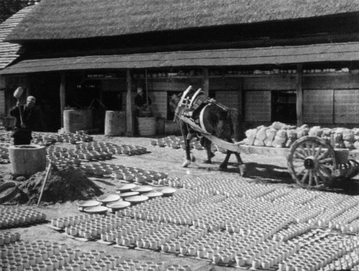 Rows of pottery laid out to dry in an outdoor workshop, with countless vessels neatly arranged in the sun beside a horse-drawn cart