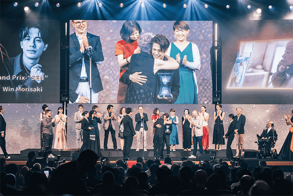 An award recipient holding a trophy on stage as others applaud