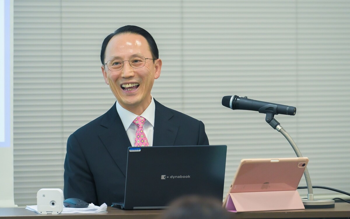 A close-up of JUNG Giyoung in a suit speaking with a bright smile during a presentation