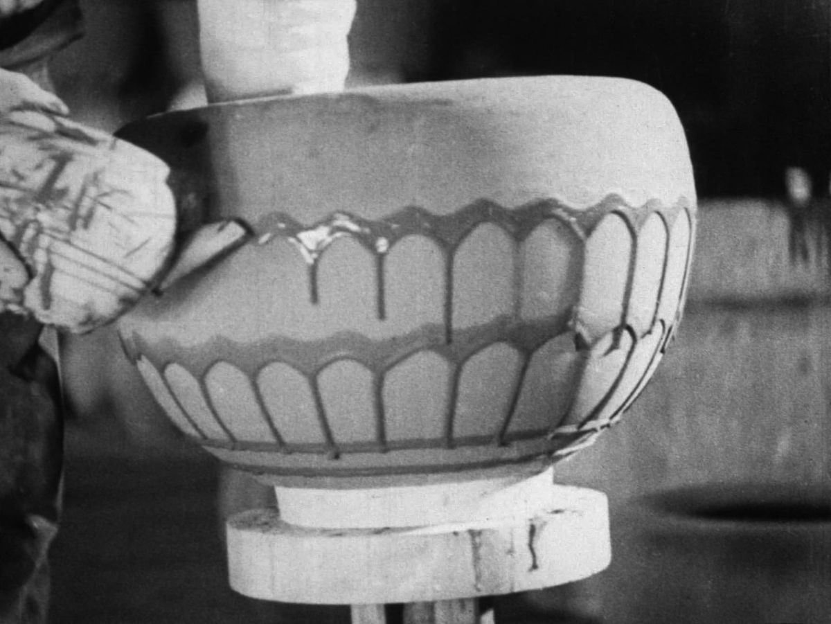 A craftsman carefully painting decorative patterns and glaze lines onto a large formed bowl