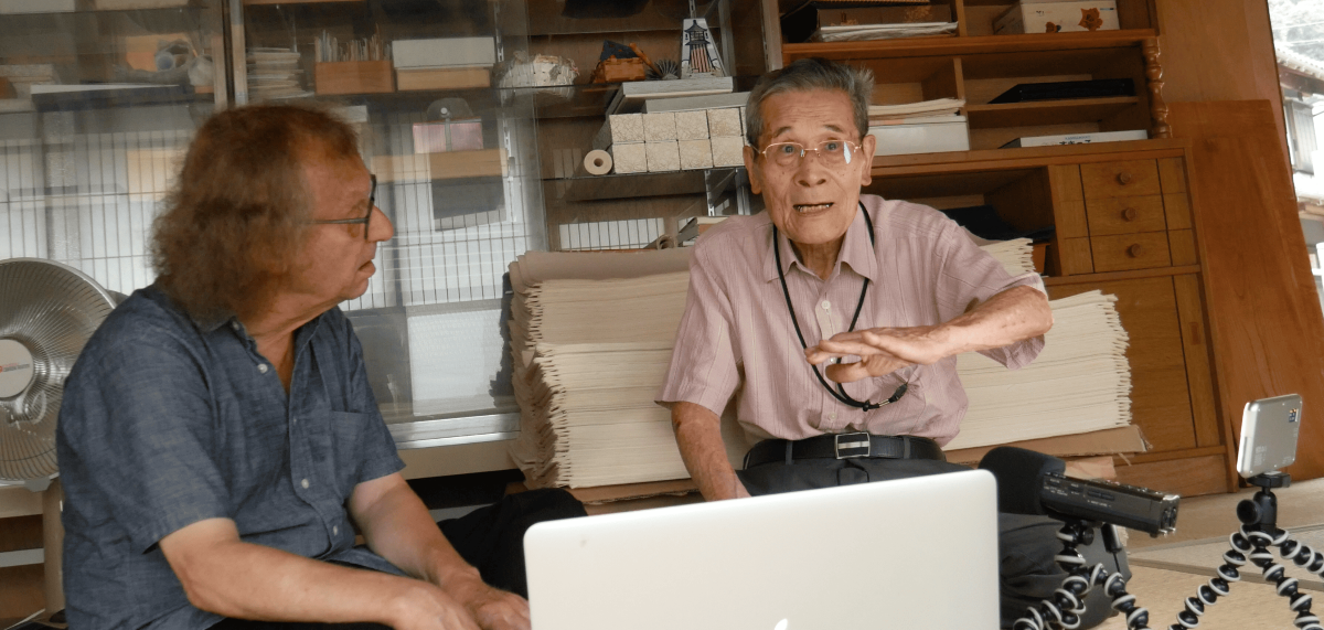 Marty Gross speaking with a Japanese paper craftsman in front of a laptop