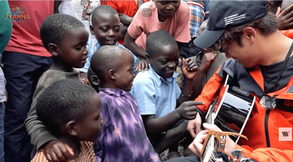 Win Morisaki playing the guitar with children in Uganda