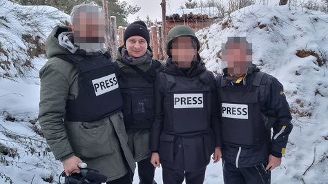 Four people wearing bulletproof vests, three of them with the word PRESS written on their chests.