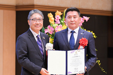 左に理事、右にバトジャルガル氏が立ち、開いた賞状を二人で持ちこちらに見せている