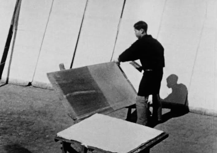 屋外で、男性が大きな板状の素材を持ち上げ、乾燥または仕上げの工程を行っている様子