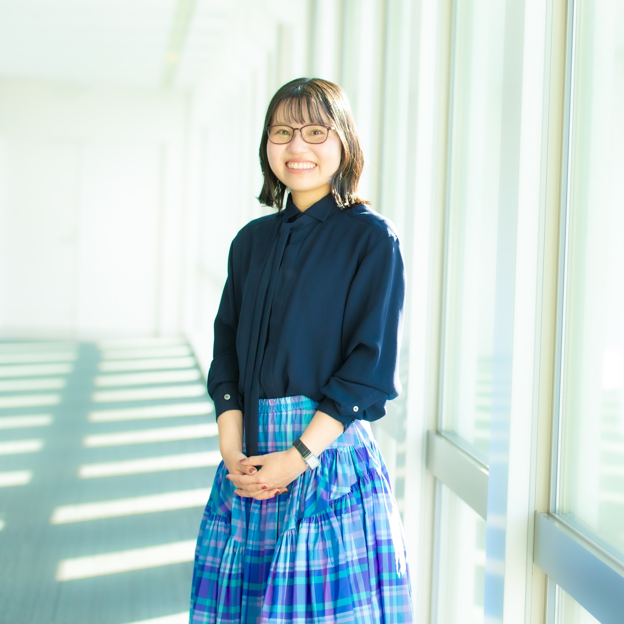 A smiling woman standing in a bright hallway with large windows