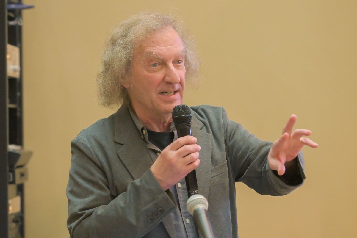 マーティ・グロス氏がマイクを持ち、身振りを交えて講演している様子