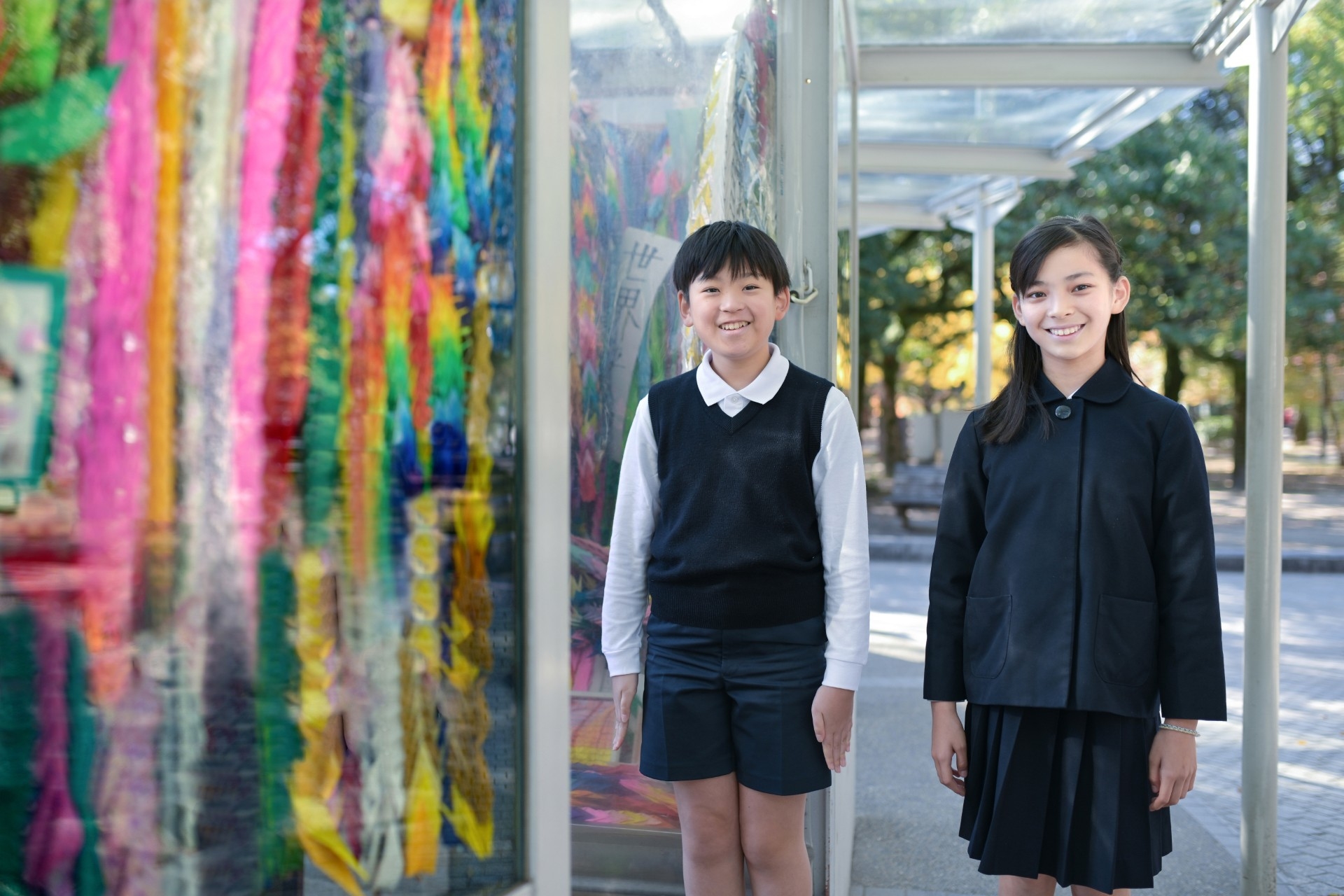 折り鶴が飾られた展示物の前に立ちこちらを見ている制服姿の児童二人